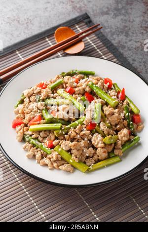 Asian food style stir-fried asparagus with minced pork and chili pepper closeup on the plate on the table. Vertical Stock Photo