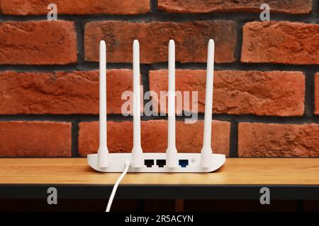 New white Wi-Fi router on wooden table near brick wall Stock Photo