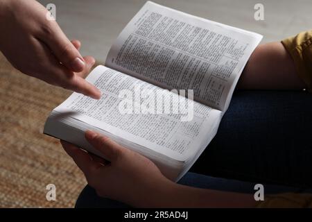 Woman showing psalm in Bible to man indoors, closeup Stock Photo