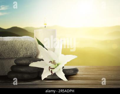 Composition with spa stones, towels and flower on wooden table against beautiful mountain landscape in morning, space for text Stock Photo