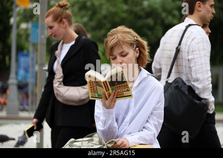 Girl sits on a street and reading book on walking people background Stock Photo