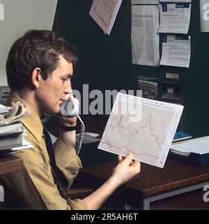 Office in the 1970s. A man is holding a document showing a chart diagram that shows the variety in sales during a certain period of time. Sweden 1971 Stock Photo