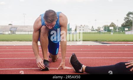 Young couple doing exercises on a running track, stretching legs and back Stock Photo
