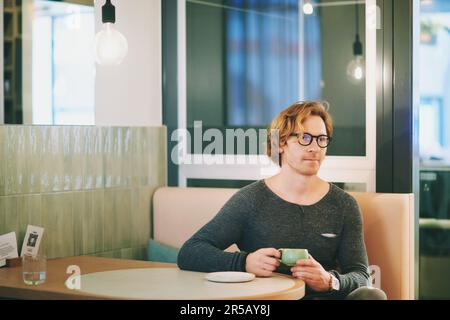 Indoor portrait of handsome red-haired young man drinking tea or coffee in cafe Stock Photo