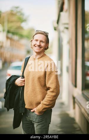 Outdoor portrait of handsome young man wearing beige fuzzy fleece sweater, posing on city street background Stock Photo