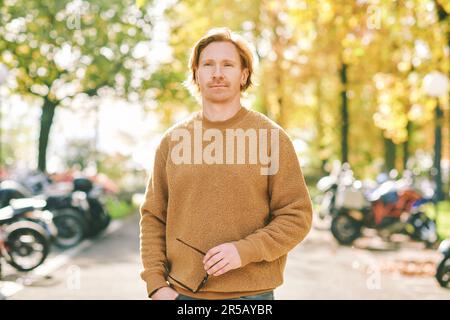 Outdoor autumn portrait of handsome young man wearing brown fuzzy fleece sweater, holding sunglasses in hands Stock Photo