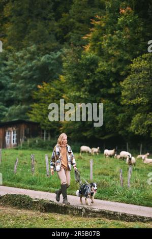 Farm landscape, young woman walking with australian shepherd dog Stock Photo