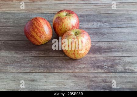 Three fresh, juicy apples are placed on a rustic wooden cutting board situated on a wooden table, ready to be enjoyed Stock Photo
