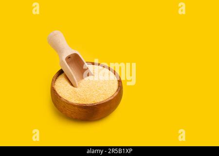 Cornmeal in a wooden bowl with a wooden spoon on a yellow background with copy space Stock Photo