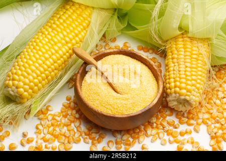 Pieces of corn and cornmeal in a wooden bowl on a white background in a top view Stock Photo