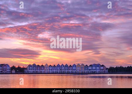 Purple skies and sunset over lake De Rietplas in Houten in the Netherlands. Row of colourful wooden newly built Dutch houses in the distance. Stock Photo
