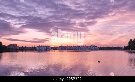 Purple skies and sunset over lake De Rietplas in Houten in the Netherlands. Row of colourful wooden newly built Dutch houses in the distance. Stock Photo