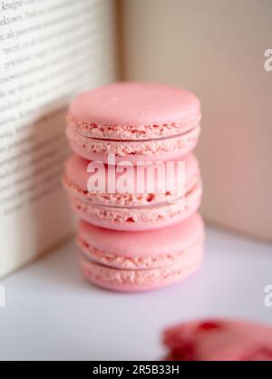 Stack of three pink macarons and one bitten pink macaron in the front with book in background Stock Photo