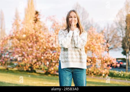 Outdoor portrait of young happy blond woman in spring park, emotional female model having fun on sunny warm day, holding hands next to face, looking a Stock Photo