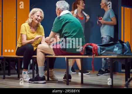 Mature man and woman facing each other while sitting in gym locker room and talking before training. Health concept. Stock Photo