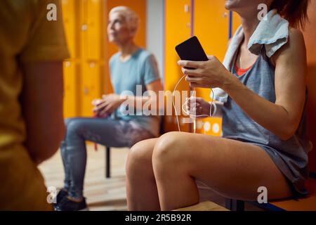 Three woman in gym locker room sitting and talking after workout. Health, wellbeing, lifestyle concept. Stock Photo