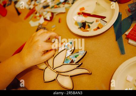 Closeup of female hand making a mosaic. The process of creating of a mosaic shape in the form of a lotus. Glass cutter, multi colored pieces of glass Stock Photo