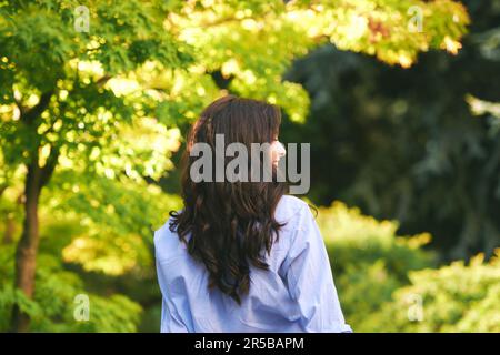 Outdoor portrait of happy young woman enjoying environment in green park, back view Stock Photo