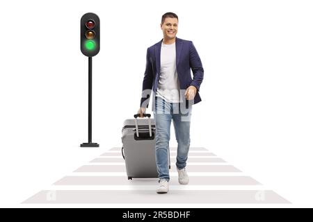 Full length portrait of a man smiling and walking with a suitcase at a pedestrian crossing isolated on white background Stock Photo