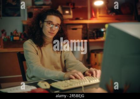 Portrait of young programmer in eyeglasses looking at camera while developing new software on computer at table Stock Photo