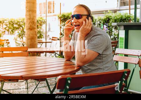 middle-aged man, elegant, modern, wearing headphones sits in street cafe Stock Photo