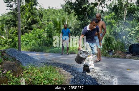 A construction worker mixes cement, asphalt, and gravel while working on a road repair project Stock Photo