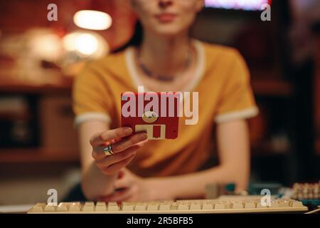 Close-up of young woman saving information on floppy disk while working on computer Stock Photo