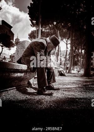 A lonely old man in a suit and hat sitting on a park bench contemplating life. Stock Photo