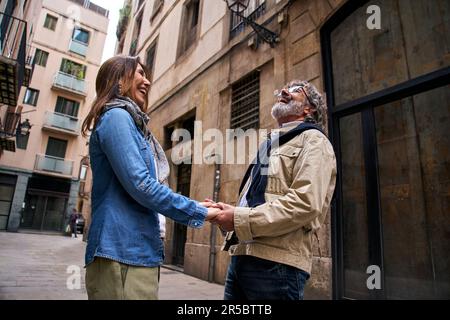 Smiling mature couple of cheerful retirees holding hands on city street. Happy adult love couple. Stock Photo