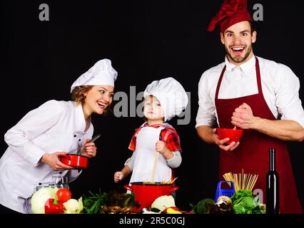 Happy family in chef uniform preparing breakfast, dinner or supper. Healthy food at home. Parents teaching little boy to cook. Mother, father and son Stock Photo