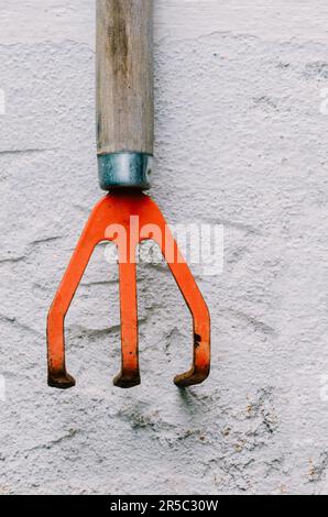 A bright orange rusty garden tool hanging on a white wall Stock Photo