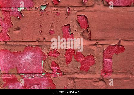 Red paint peeling off over brickwork to reveal pink paint underneath Stock Photo