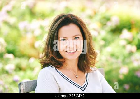 Outdoor portrait of beautiful 40 - 45 years old woman sitting on bench ib green park, healthy lifestyle Stock Photo