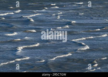 Long breaking waves on the shore with the white waves lit by the sun Stock Photo