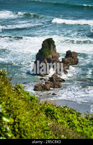 A picturesque tropical beach featuring large rocks and crystal clear waves crashing on the shore, creating a stunning landscape Stock Photo