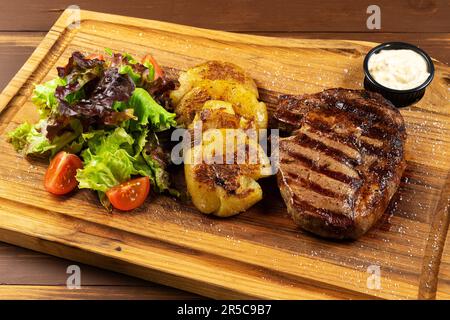 Grilled Rib Eye Black Angus served with fries, green salad and sauce on wooden background. Stock Photo
