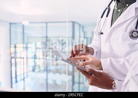 Using technology to advance medicine. two unrecognizable doctors working on a digital tablet while standing in the hospital. Stock Photo