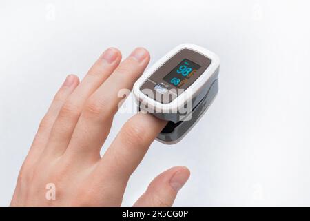 The young man's hand measures the level of oxygen in the blood using a medical device pulse oximeter on a white background. Stock Photo
