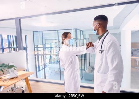 Greeting one another in the safest way possible. two unrecognizable doctors wearing masks and elbow bumping while standing in the hospital. Stock Photo