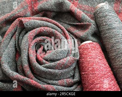 Woven red and gray tweed scarf or shawl and two bobbins with threads. Everyday warm clothes Stock Photo