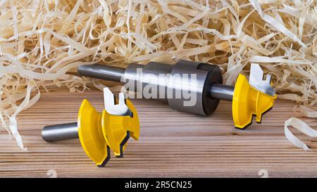 Shaping shank router bits on wood with shavings pile background. Yellow steel cutting tools with teeth on sharp edge and extension rod on wooden board. Stock Photo