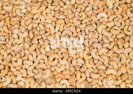 Delicious salted roasted cashews in texture pattern. Anacardium occidentale. Closeup of many cashew nuts of kidney shape in beige culinary background. Stock Photo