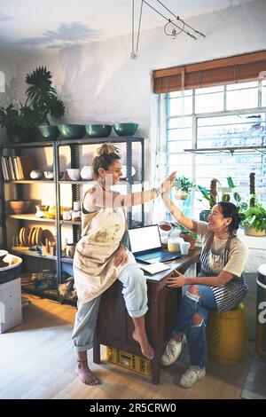 A great small business is built on big team spirit. two young women giving each other a high five in a pottery studio. Stock Photo