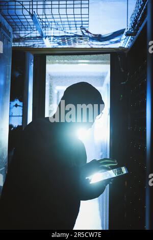 I work best in the dark. a hacker using a digital tablet in a server room. Stock Photo