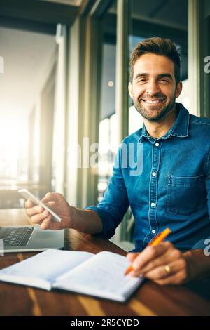 Technology allows us to work from anywhere. Cropped portrait of a handsome young businessman sitting alone and making notes while using his cellphone Stock Photo