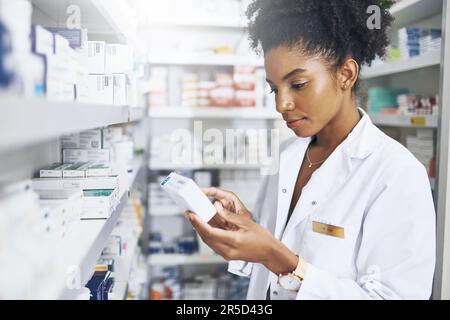Making sure the medication is safe for her customer. a pharmacist reading the label on a product in a drugstore. Stock Photo