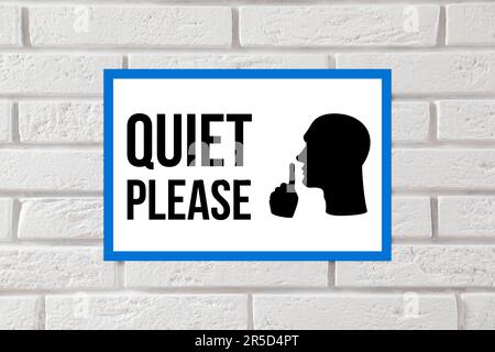 Quiet Please sign with shush gesture image on white brick wall Stock Photo