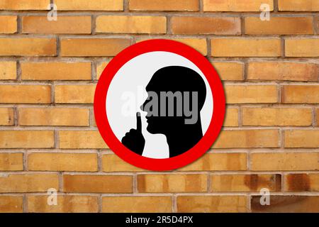 Quiet Please sign with shush gesture image on orange brick wall Stock Photo