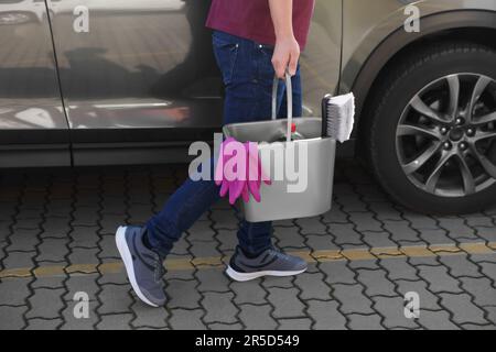 Man holding bucket with car cleaning products outdoors, closeup Stock Photo