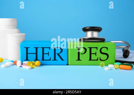 Word Herpes made of colorful cubes, different pills and stethoscope on light blue background Stock Photo